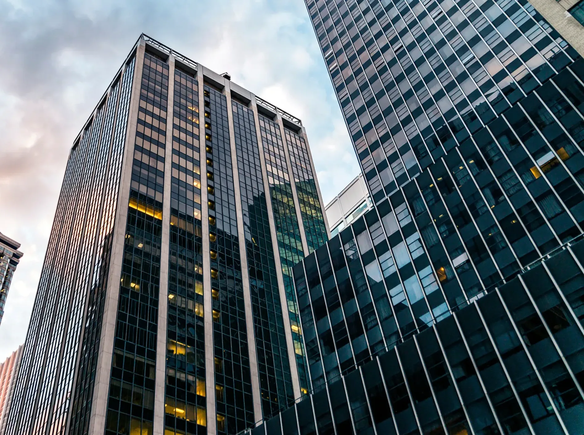 Home Tall glass and steel office buildings reflecting the sky, viewed from street level with some lights on inside—much like the kind of thriving corporate environments where Silicon Valley CFTC whistleblower attorneys help protect clients and uphold justice.