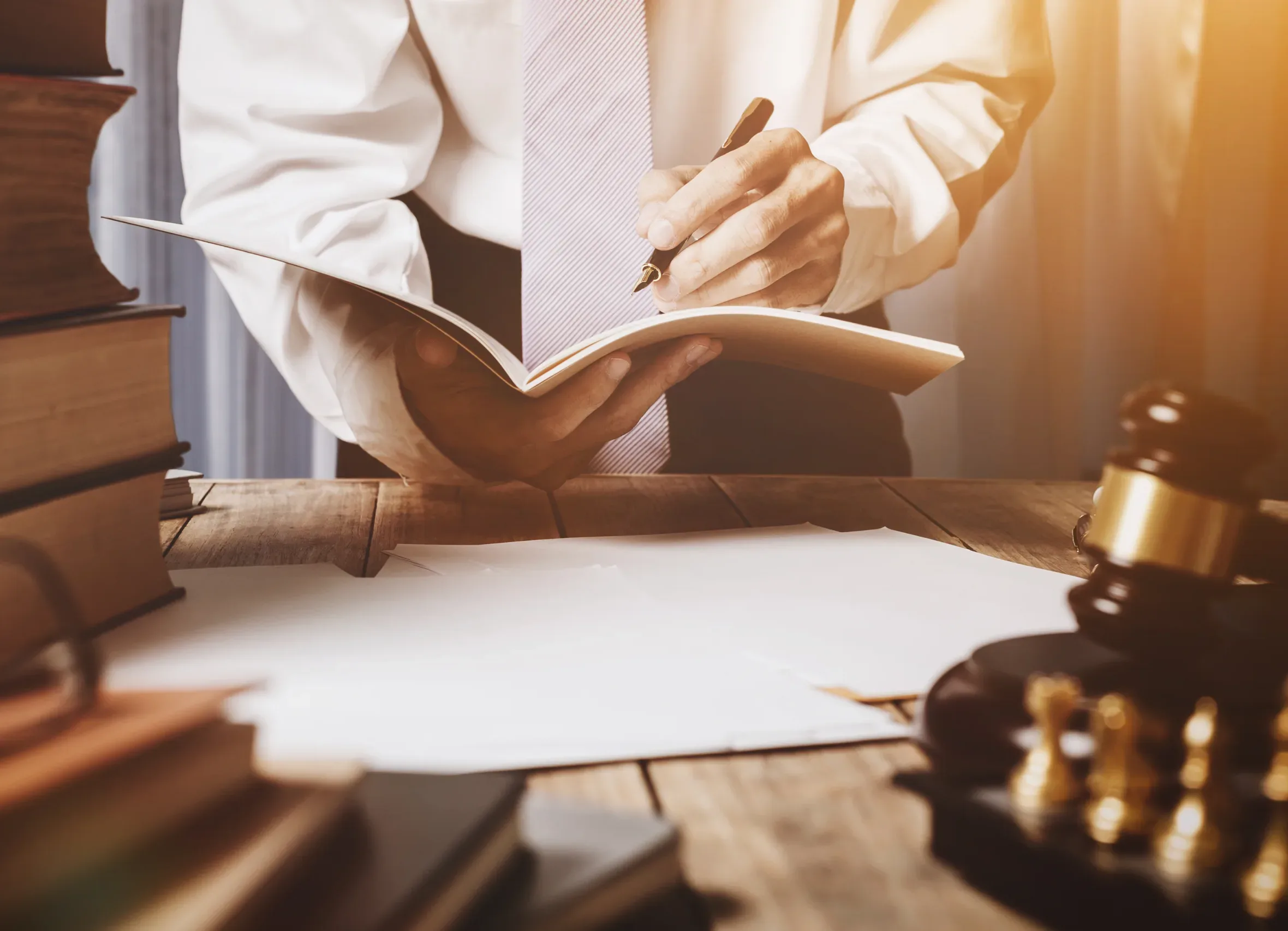 Home A person in business attire writes in an open notebook at a desk with legal books, papers, a gavel, and handcuffs—illustrating the meticulous work of New York City tax whistleblower lawyers or Silicon Valley CFTC whistleblower attorneys dedicated to justice and accountability.