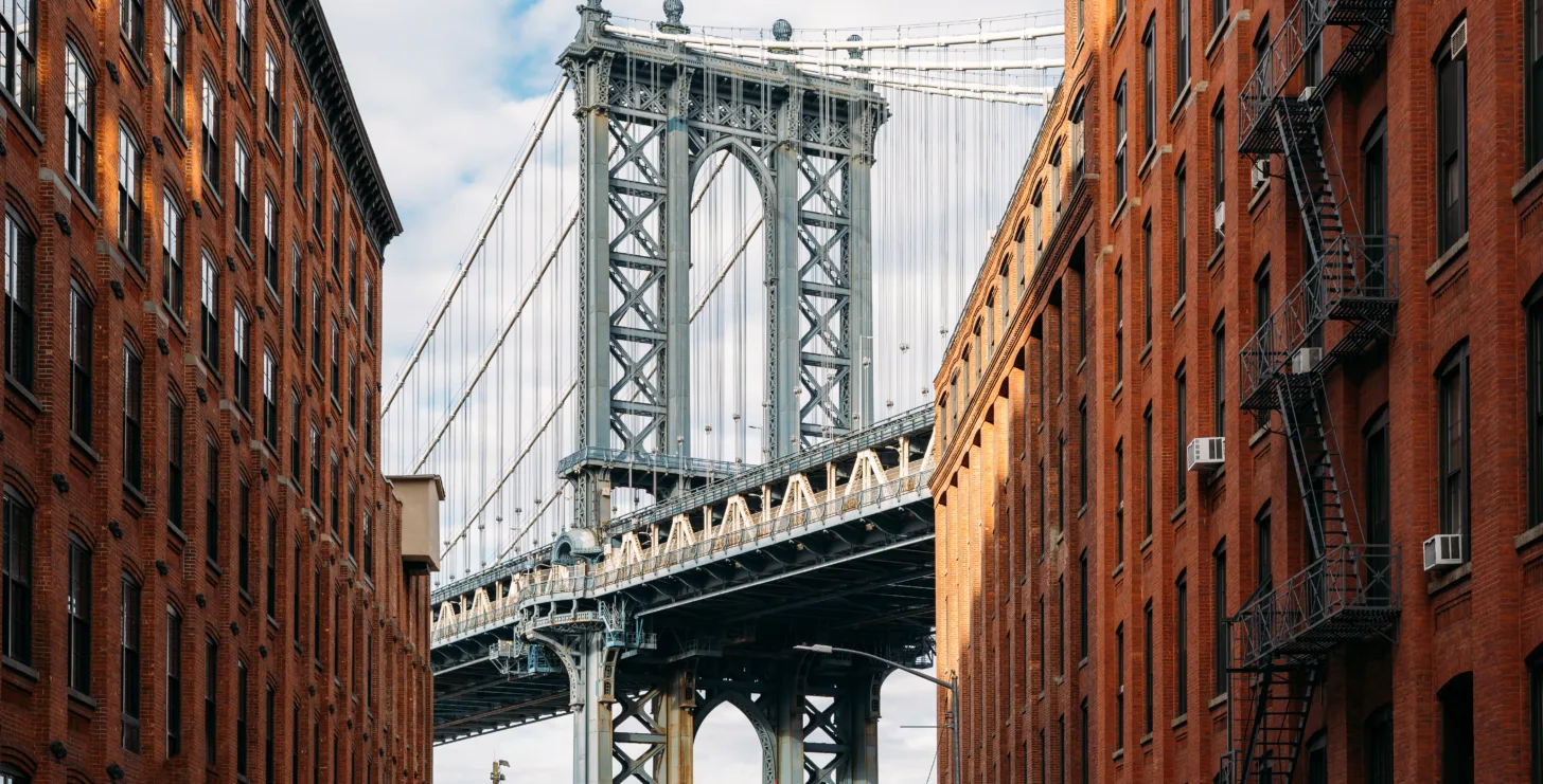 View of the Manhattan Bridge framed by two red brick buildings, with blue sky and clouds in the background—a setting where a New York Medicare whistleblower might find inspiration to stand up for justice amid the city’s enduring spirit.