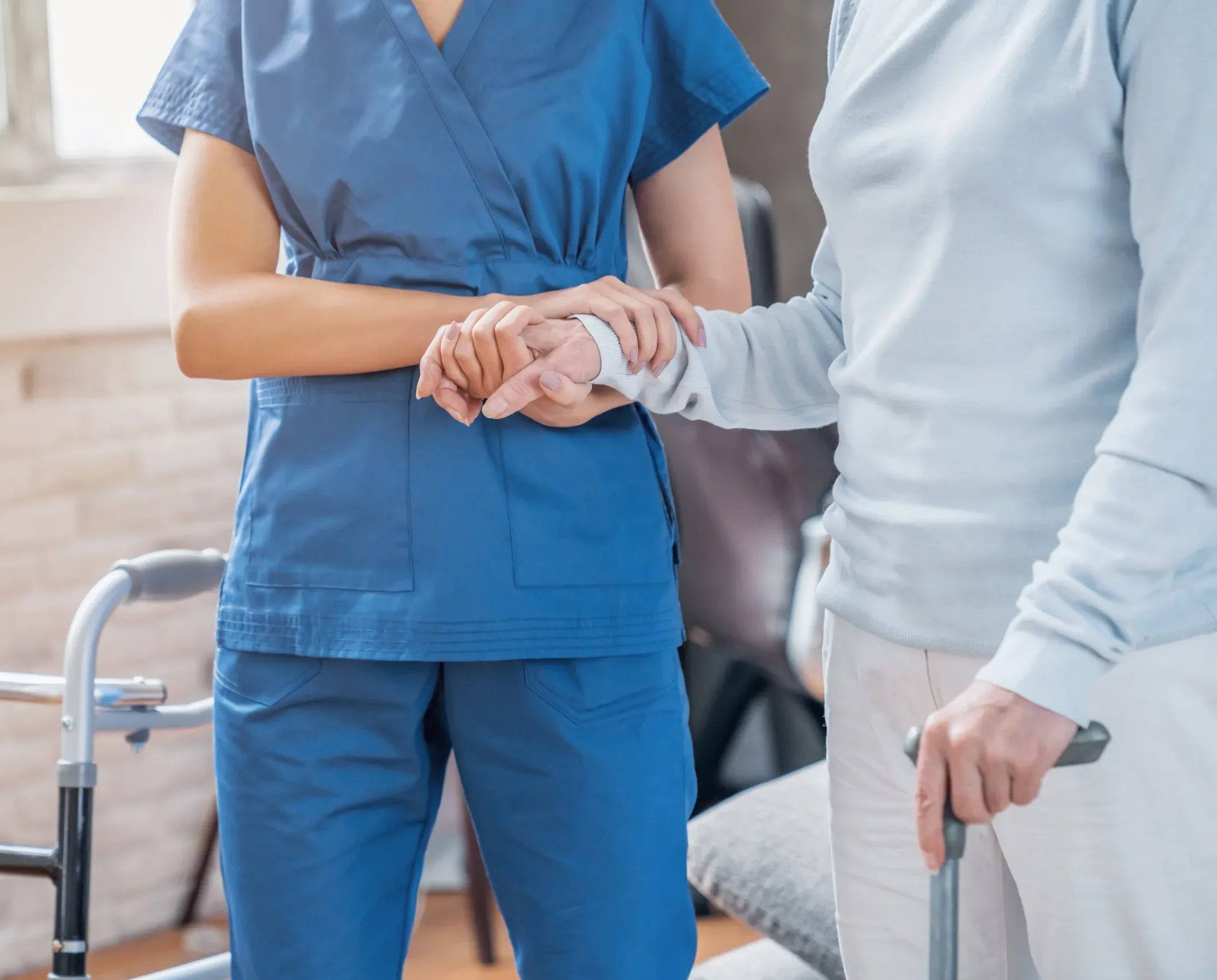 Home A healthcare worker in blue scrubs assists an older adult, who is using a cane and a walker. While their faces are not visible, scenes like this may become important when consulting a San Francisco healthcare fraud lawyer to ensure proper care and compliance.