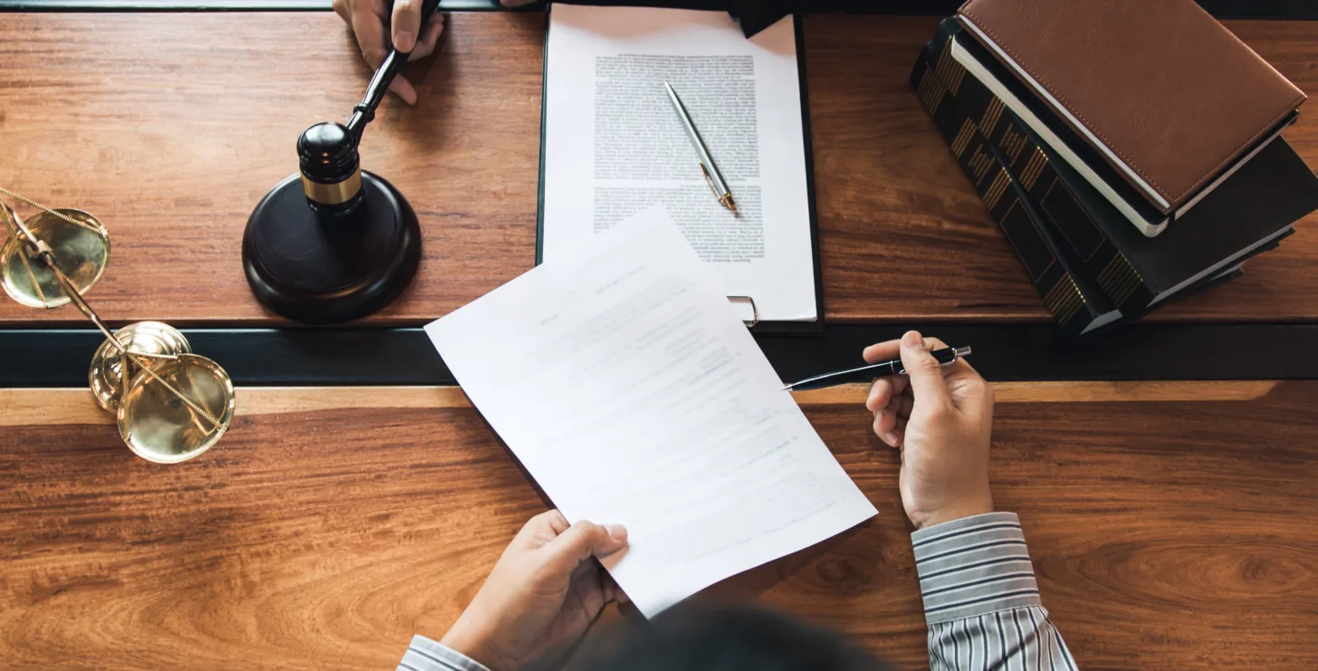 Three people at a wooden table review legal documents with a gavel, law book, and scales of justice present—a scene reminiscent of consultations with experienced Silicon Valley CFTC whistleblower attorneys.