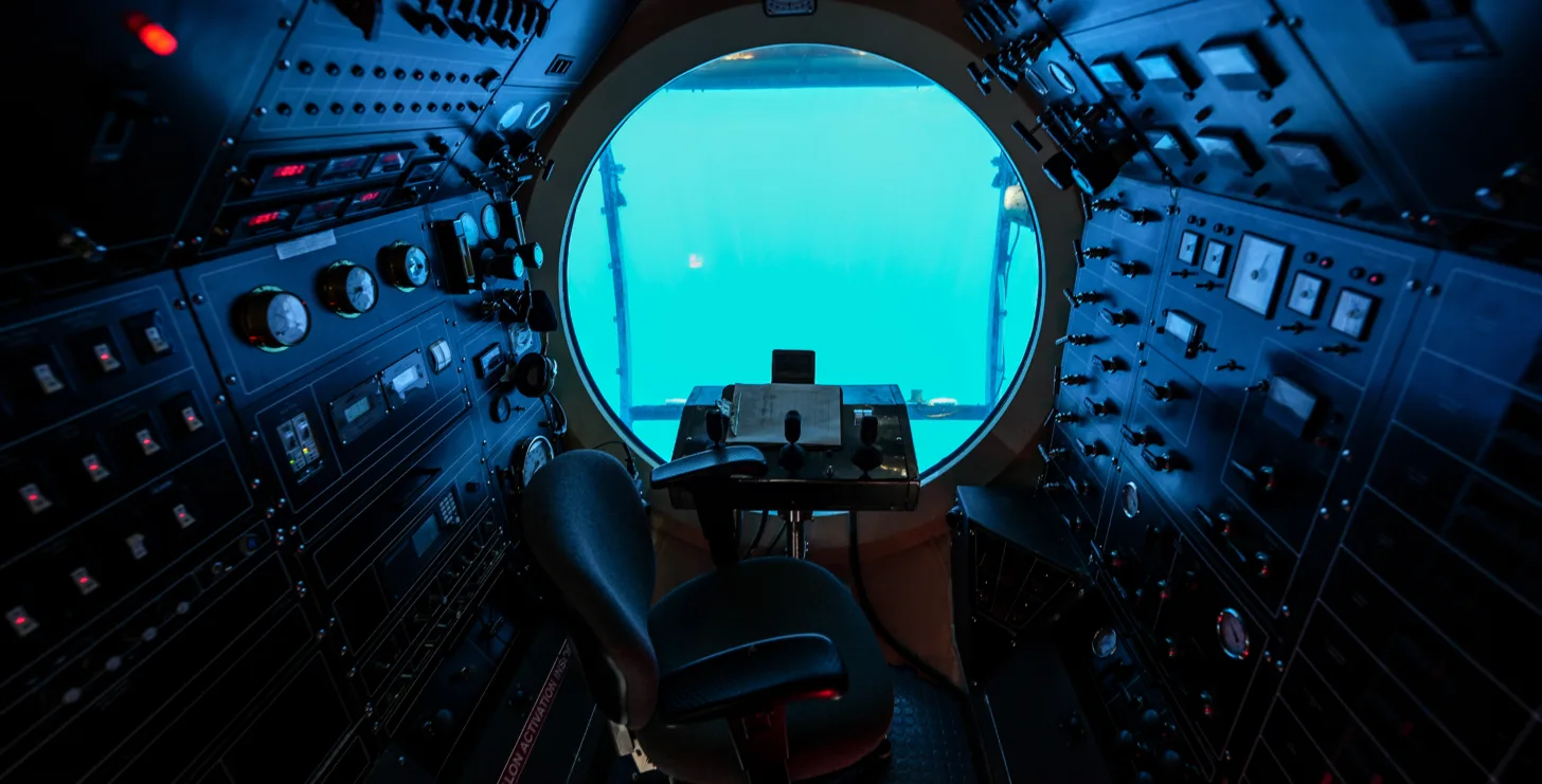 Interior of a submarine control room with a central chair, control panels on both sides, and a large circular window showing an underwater view—an environment as diligent and focused as a New York City tax whistleblower lawyer investigating hidden details in the depths of financial systems.