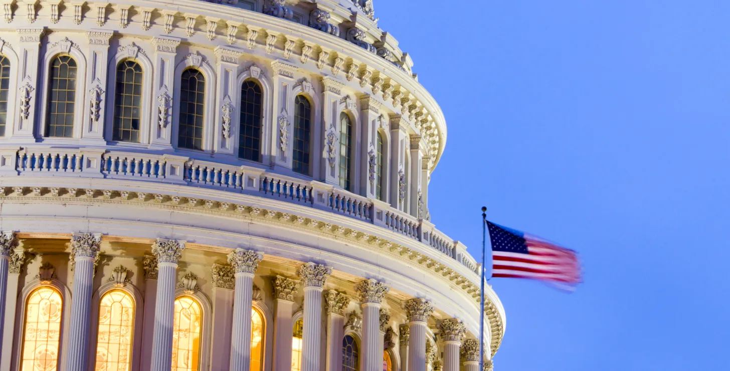 Close-up of the U.S. Capitol building dome with illuminated windows at dusk, and an American flag waving in the foreground—a powerful symbol of justice that resonates with dedicated New York City tax whistleblower lawyers advocating for transparency across the nation.