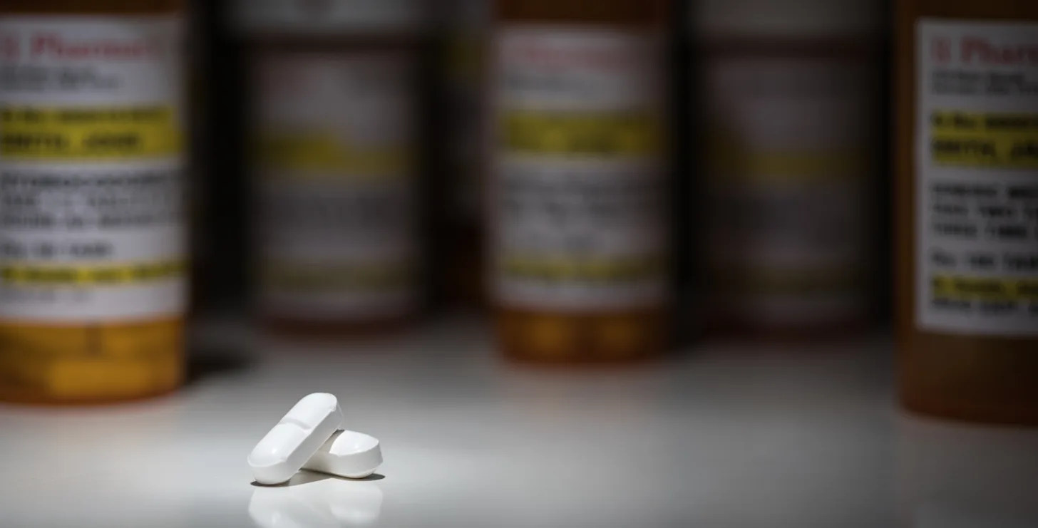 Two white pills are placed on a smooth surface in focus, with several blurred prescription pill bottles in the background—an image reminiscent of cases handled by a dedicated San Francisco healthcare fraud lawyer.