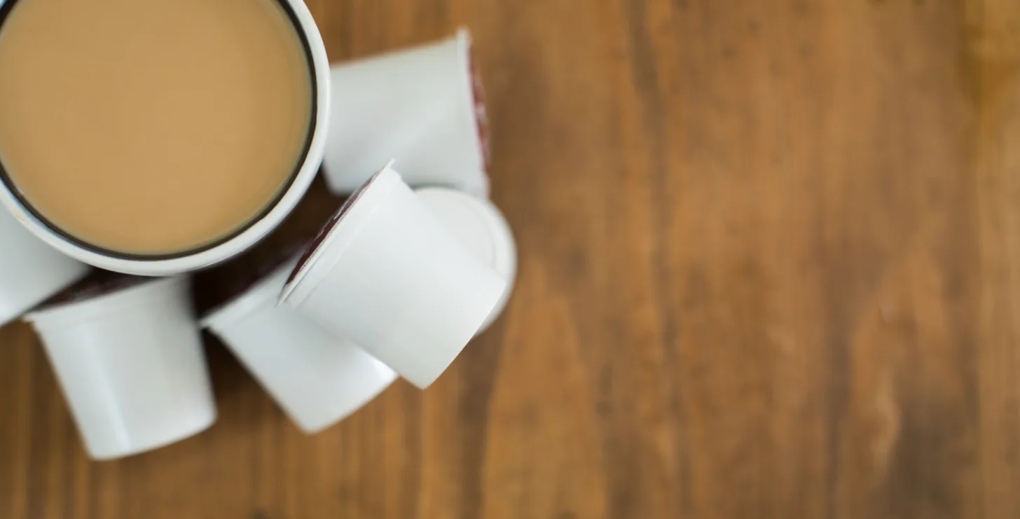 A cup of coffee with cream sits on a wooden table, surrounded by several single-serve coffee creamer pods—a quiet moment that could inspire anyone, from a Boston government contract fraud attorney reviewing case files to a New York City tax whistleblower lawyer preparing vital documents.
