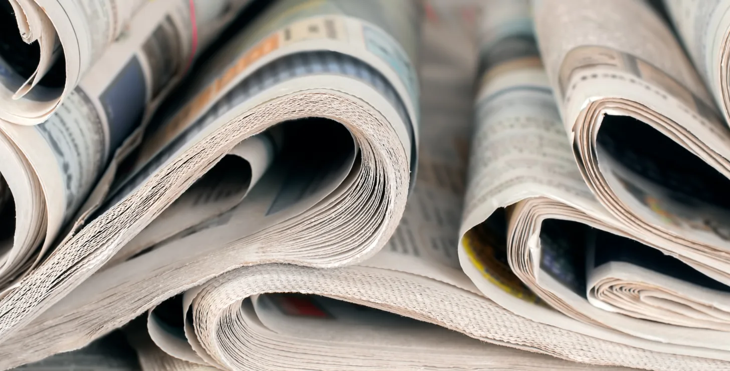 Close-up view of several folded newspapers stacked side by side, showing the curved edges of the pages and printed text and images inside—perhaps featuring headlines about a San Francisco healthcare fraud lawyer or updates on Silicon Valley CFTC whistleblower attorneys making news.