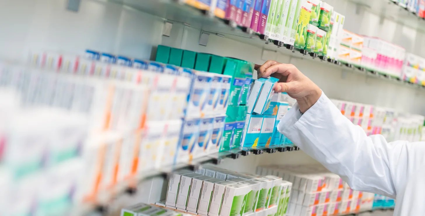 A pharmacist selects a box of medication from shelves stocked with various pharmaceutical products in a pharmacy, much like how a San Jose IRS whistleblower lawyer carefully searches for crucial information amidst complex regulations and documents.