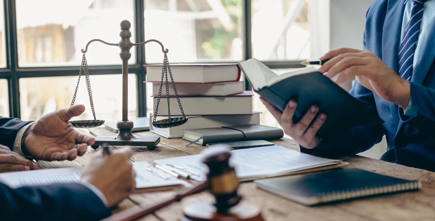 Two people in suits discuss legal documents at a desk with books, a scale of justice, and a gavel, in an office with large windows—reflecting the professionalism and focus of Silicon Valley CFTC whistleblower attorneys.