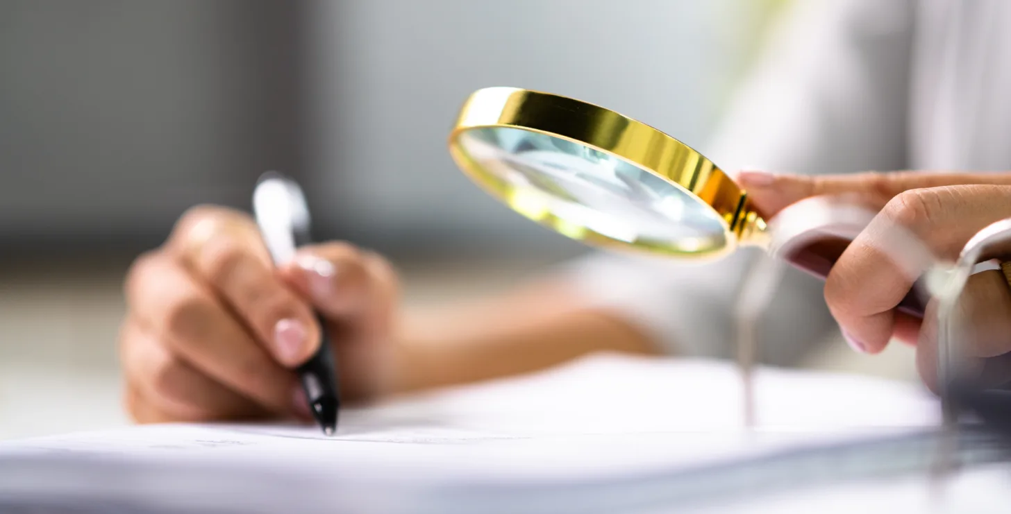 Person holding a magnifying glass and pen, closely examining documents on a desk—evoking the diligence of a New York Medicare whistleblower meticulously reviewing crucial evidence.
