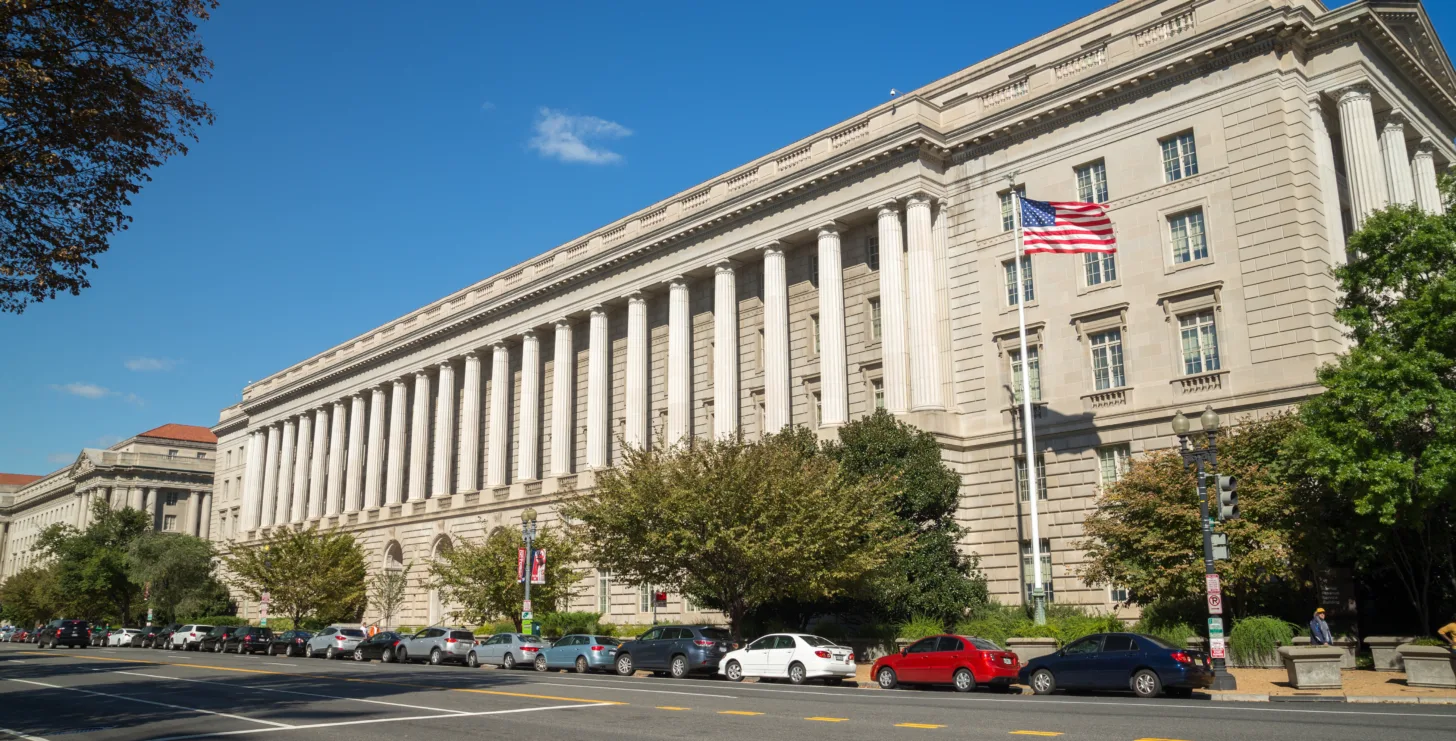 Large government building with columns, an American flag, and cars parked along the street under a clear blue sky—an iconic setting where San Jose IRS whistleblower lawyers may advocate for justice.