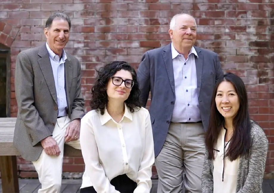 Four people, two men and two women, pose together outdoors in front of a brick wall, all wearing business casual attire and looking at the camera. The group exudes professionalism, resembling a dedicated team of San Jose IRS whistleblower lawyers ready to advocate for clients with integrity and expertise.