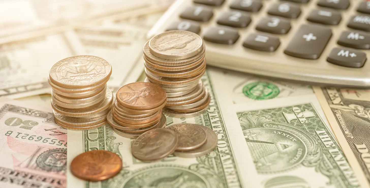 Stacks of coins and assorted U.S. dollar bills are spread out next to a calculator on a flat surface, evocative of the detailed financial reviews performed by a New York City tax whistleblower lawyer.