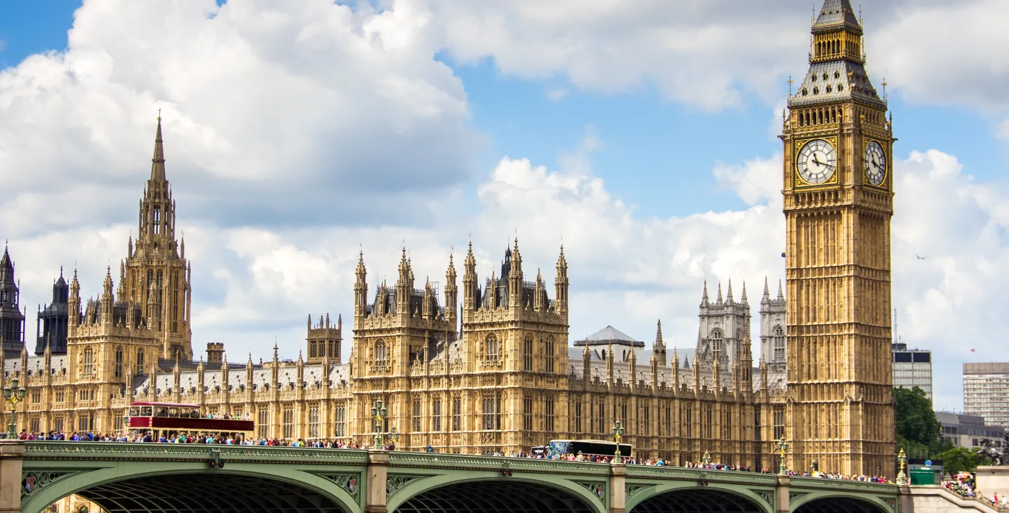 View of the Palace of Westminster and Big Ben clock tower in London with people and vehicles crossing Westminster Bridge—reminding one of how iconic landmarks, much like a dedicated New York Medicare whistleblower, stand as vigilant sentinels safeguarding public trust.