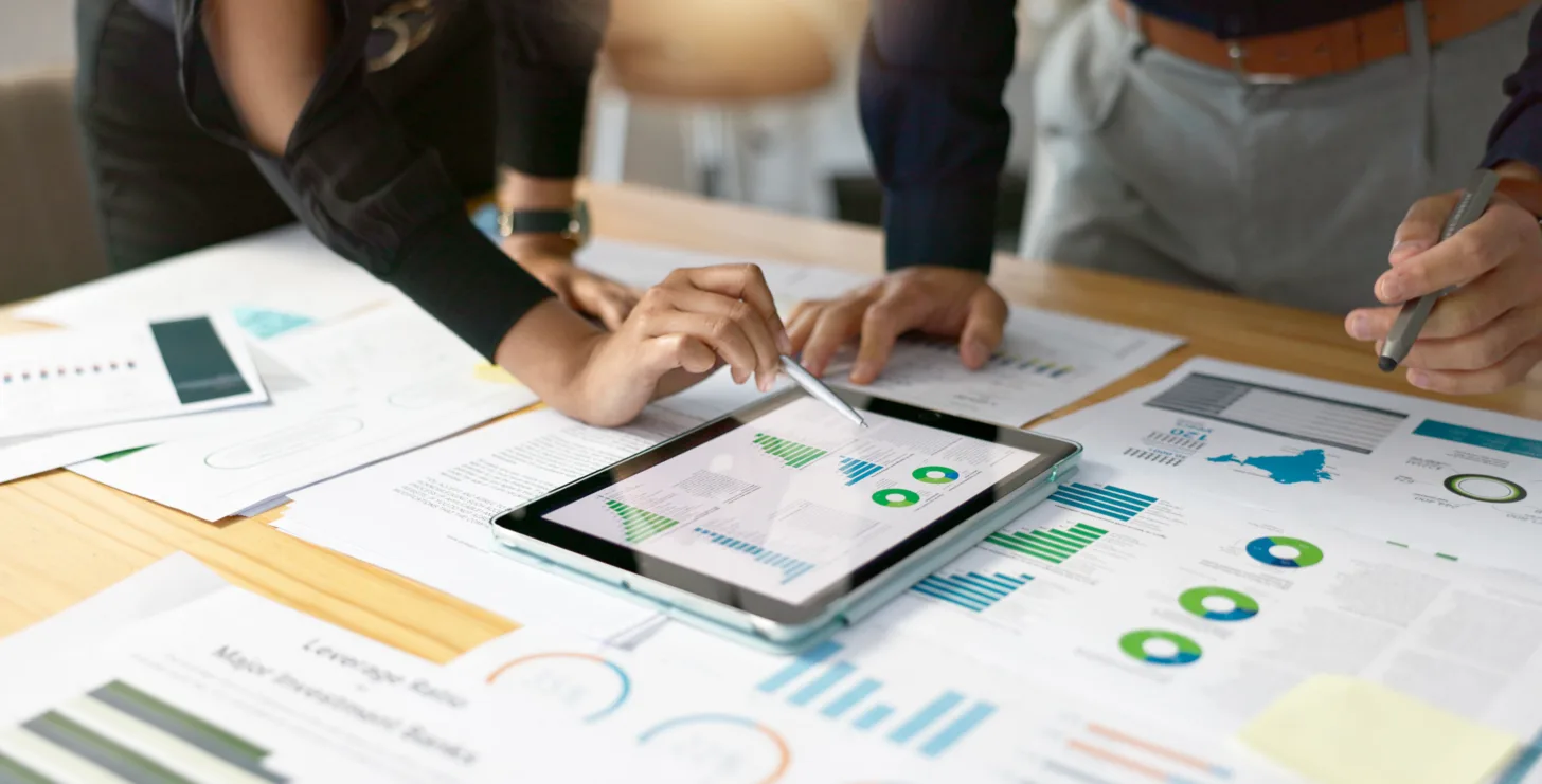 Two people, possibly San Jose IRS whistleblower lawyers, are reviewing graphs and charts on a tablet and paper documents spread across a desk in an office setting.