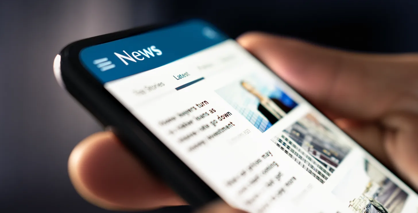 Close-up of a hand holding a smartphone displaying a news website, with headlines and images visible on the screen—perfect for staying informed on topics like Boston government contract fraud attorney updates and legal developments.