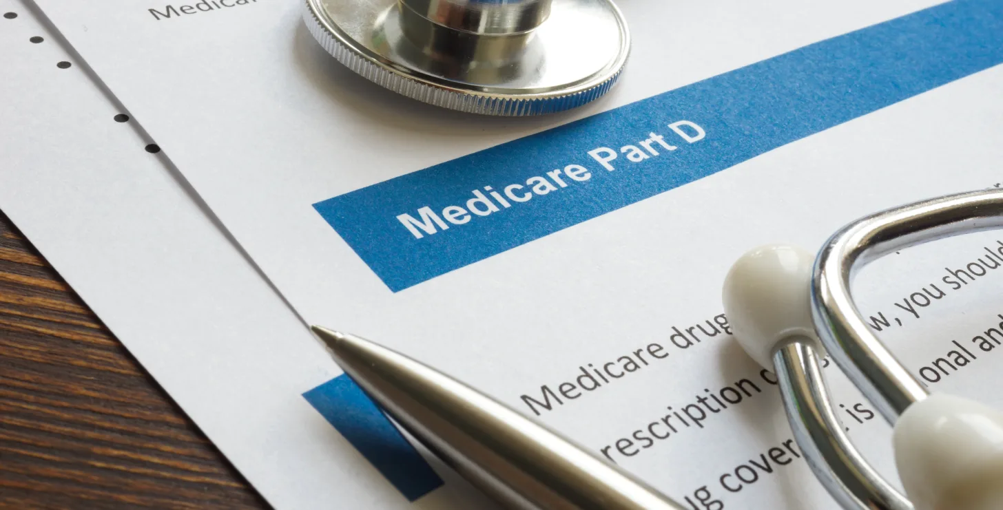 A Medicare Part D document rests on a desk, partially covered by a pen, stethoscope, and scattered papers—capturing the kind of detailed review a San Francisco healthcare fraud lawyer might conduct when investigating potential Medicare violations.