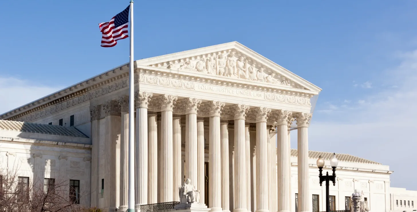 The United States Supreme Court building in Washington, D.C., is shown under a clear sky with the American flag flying on a flagpole in front—a powerful symbol of justice often familiar to any D.C. FCA whistleblower attorney.